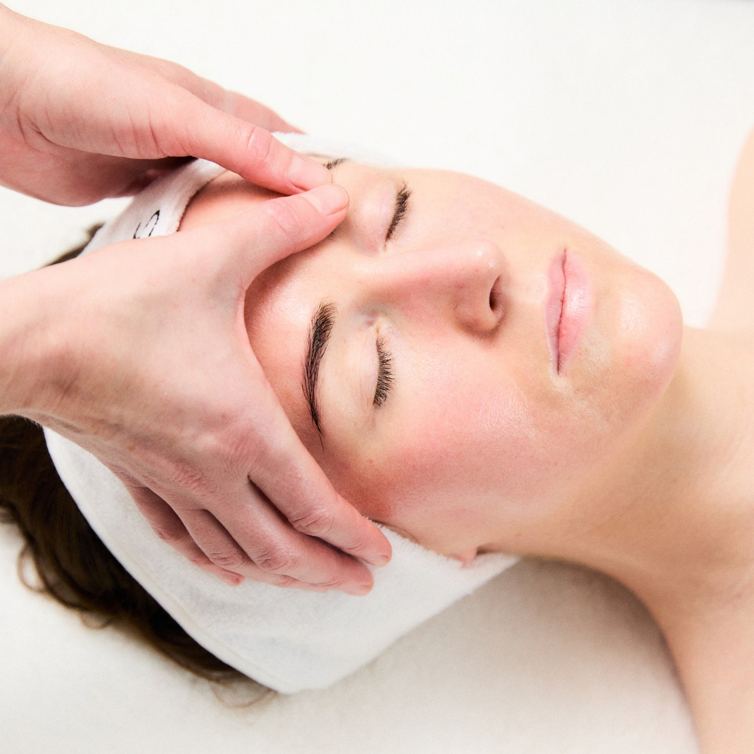Person receiving a facial massage with hands on a white background